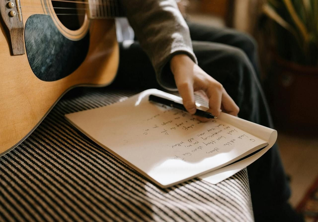 A man sits at a table, writing lyrics in a notebook, focused on his creative process.
